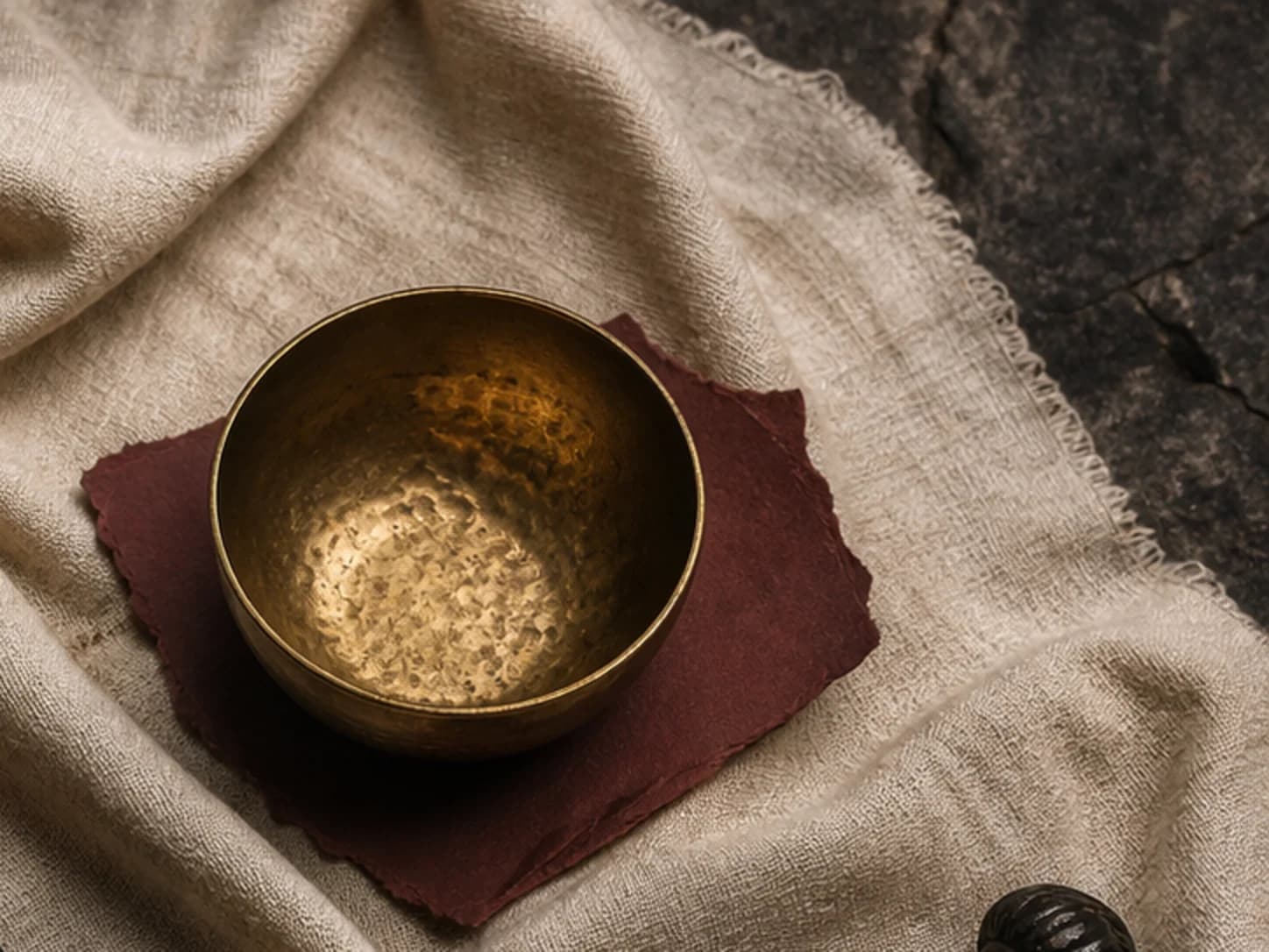 A brass cup staged on warm ivory and oxblood cloth